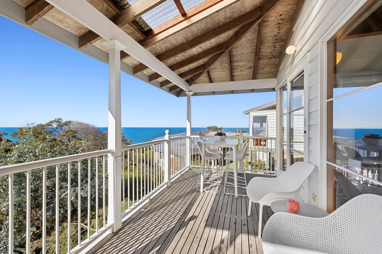 A covered outdoor area with a wooden deck, white railings, and a table with chairs.