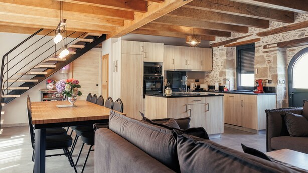 Una cucina moderna con travi in legno, una zona pranzo con tavolo e sedie in legno, e un'accogliente area relax con cuscini.
