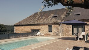 Un edificio in pietra con piscina, area relax esterna e vista sul paesaggio circostante.