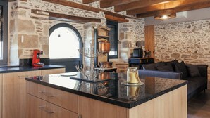 Cucina con parete in pietra, travi in legno, macchina del caffè e isola moderna con piano in vetro.