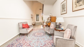 A spacious hallway with a patterned carpet, two armchairs, a small table with a lamp, and a piano.