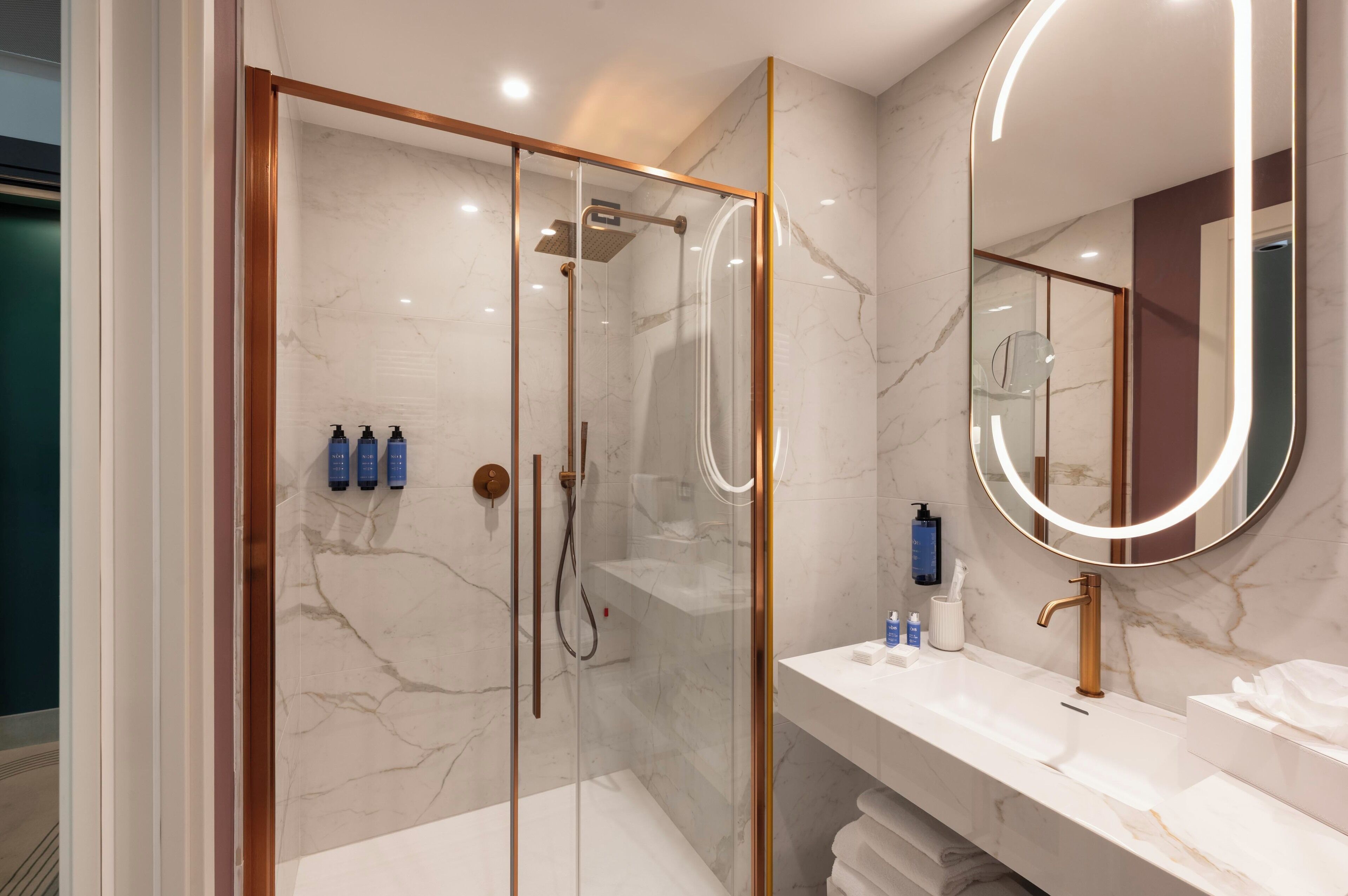A modern bathroom with a glass-enclosed shower, a marble-topped sink, and a large mirror with a circular light.