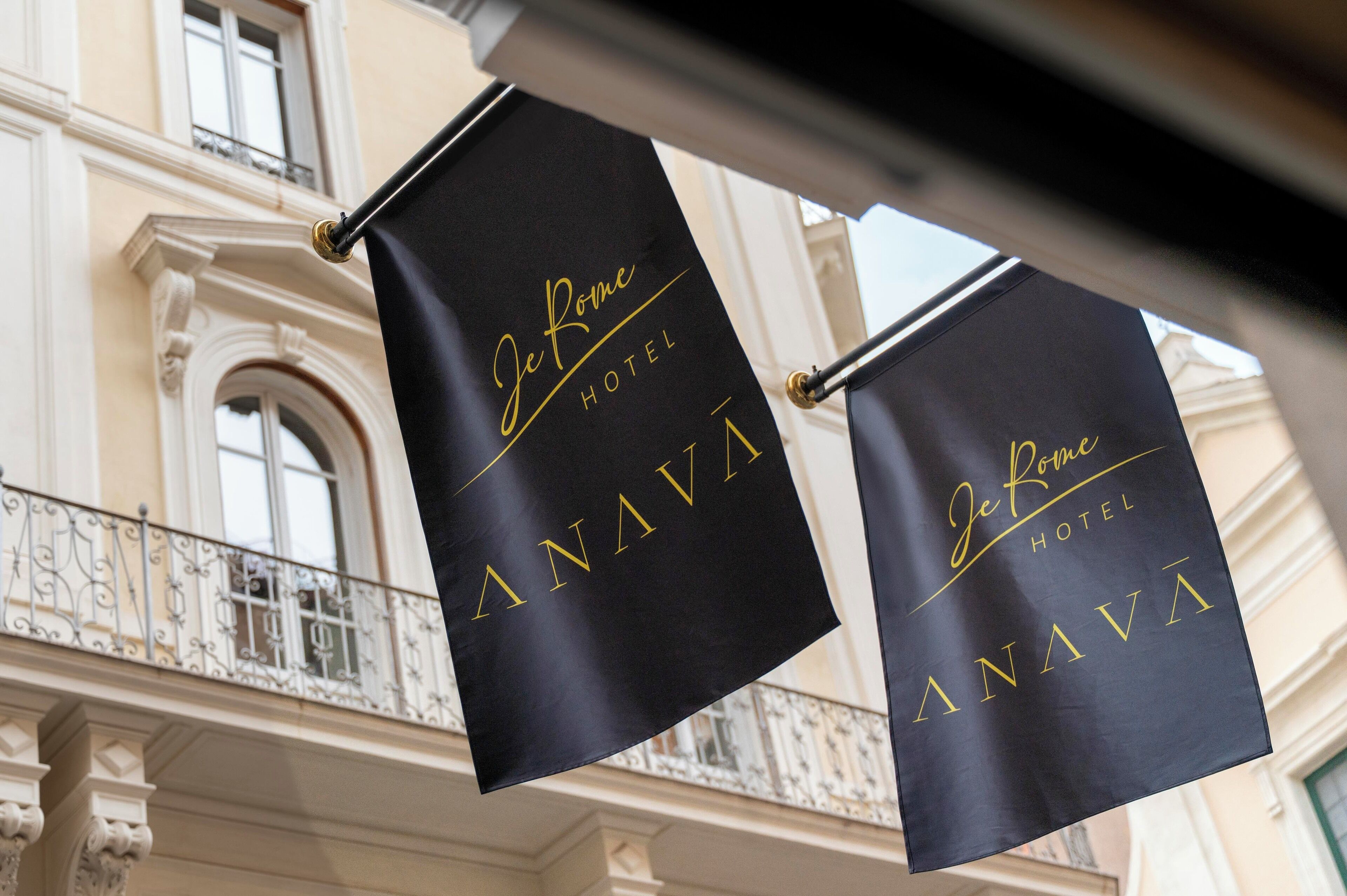 Two black banners with gold lettering hanging from a balcony railing, reading "Je Rome HOTEL ANAVA."