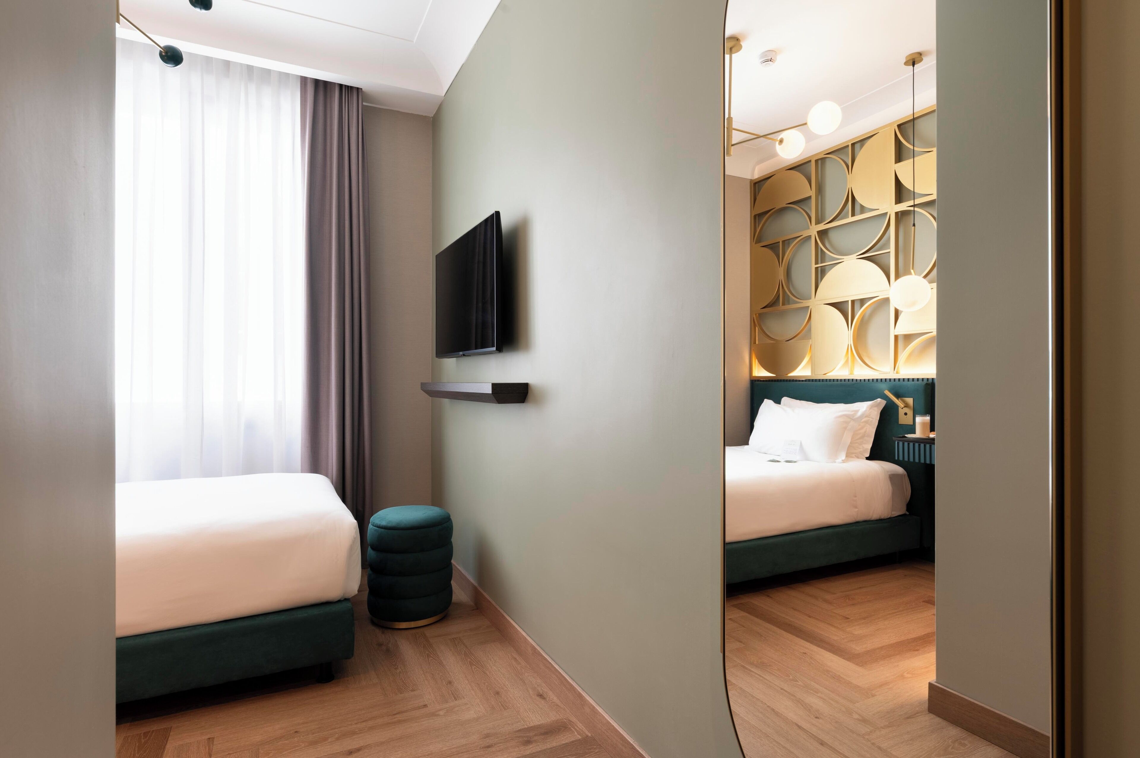 A modern hotel room with a large bed, a smaller bed, a TV mounted on the wall, and a unique geometric light fixture above the smaller bed.