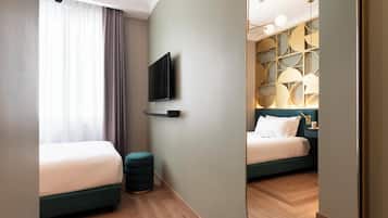A modern hotel room with a large bed, a smaller bed, a TV mounted on the wall, and a unique geometric light fixture above the smaller bed.