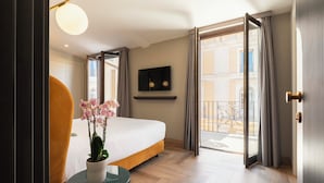 Habitación de hotel con cama, una mesita con un florero, televisor en la pared y balcón con cortinas.
