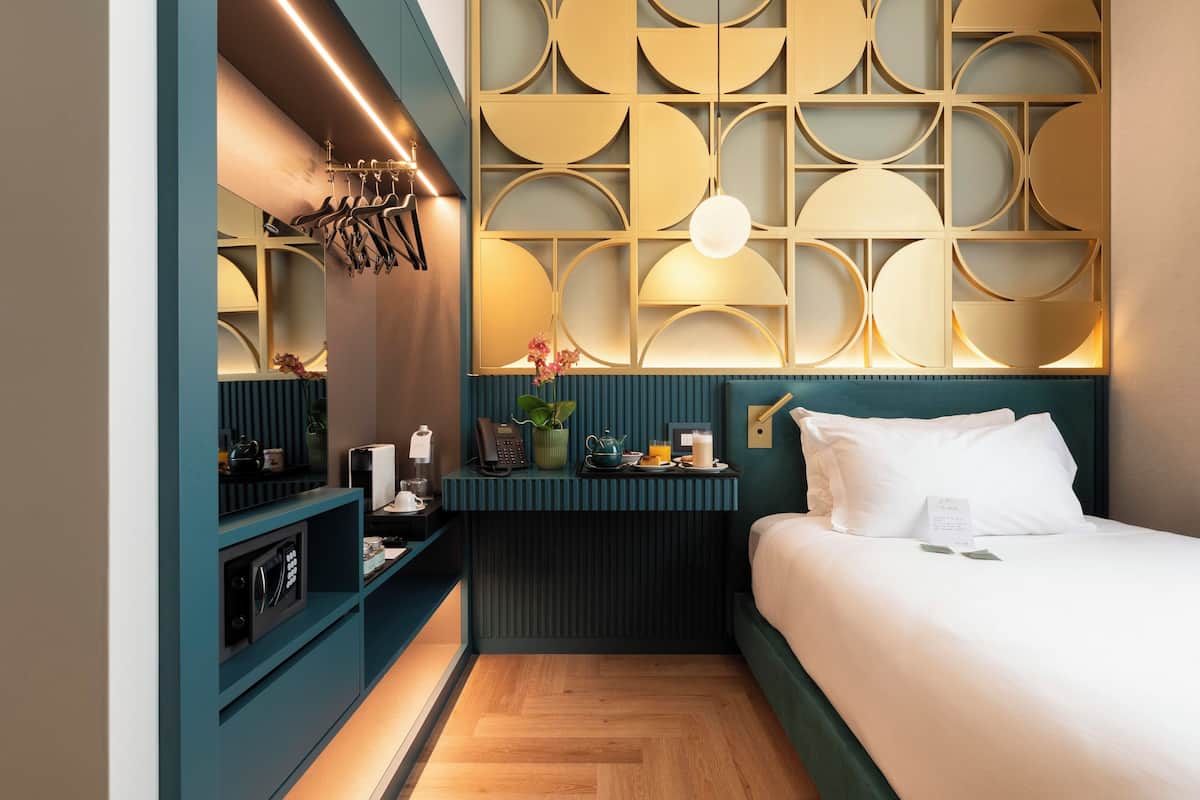 A compact hotel room with a bed, a bedside table, a wall-mounted TV, and a decorative panel with circular patterns.