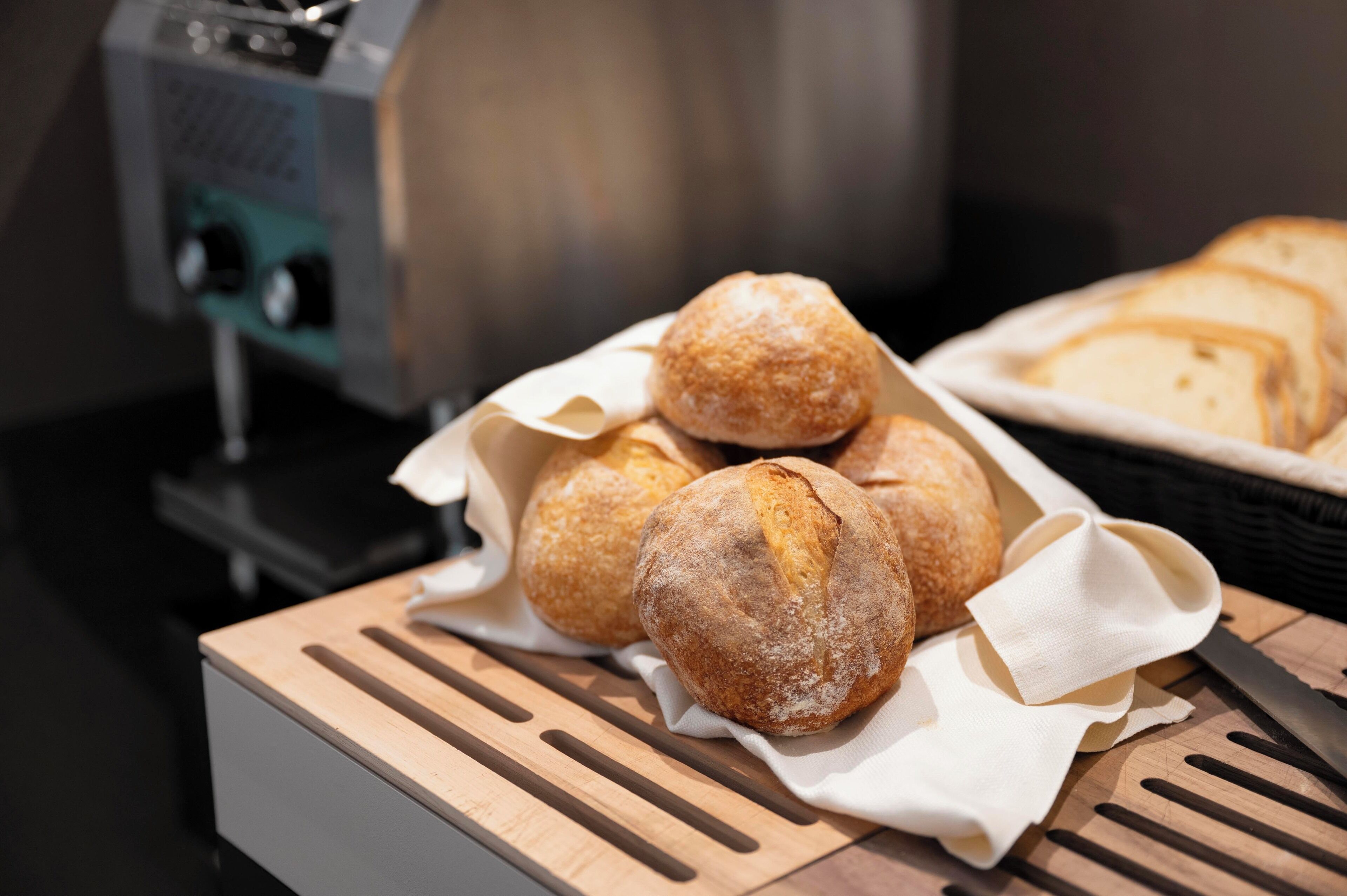 Un vassoio con pane appena sfornato su un tagliere di legno, con una bread slicer sullo sfondo.