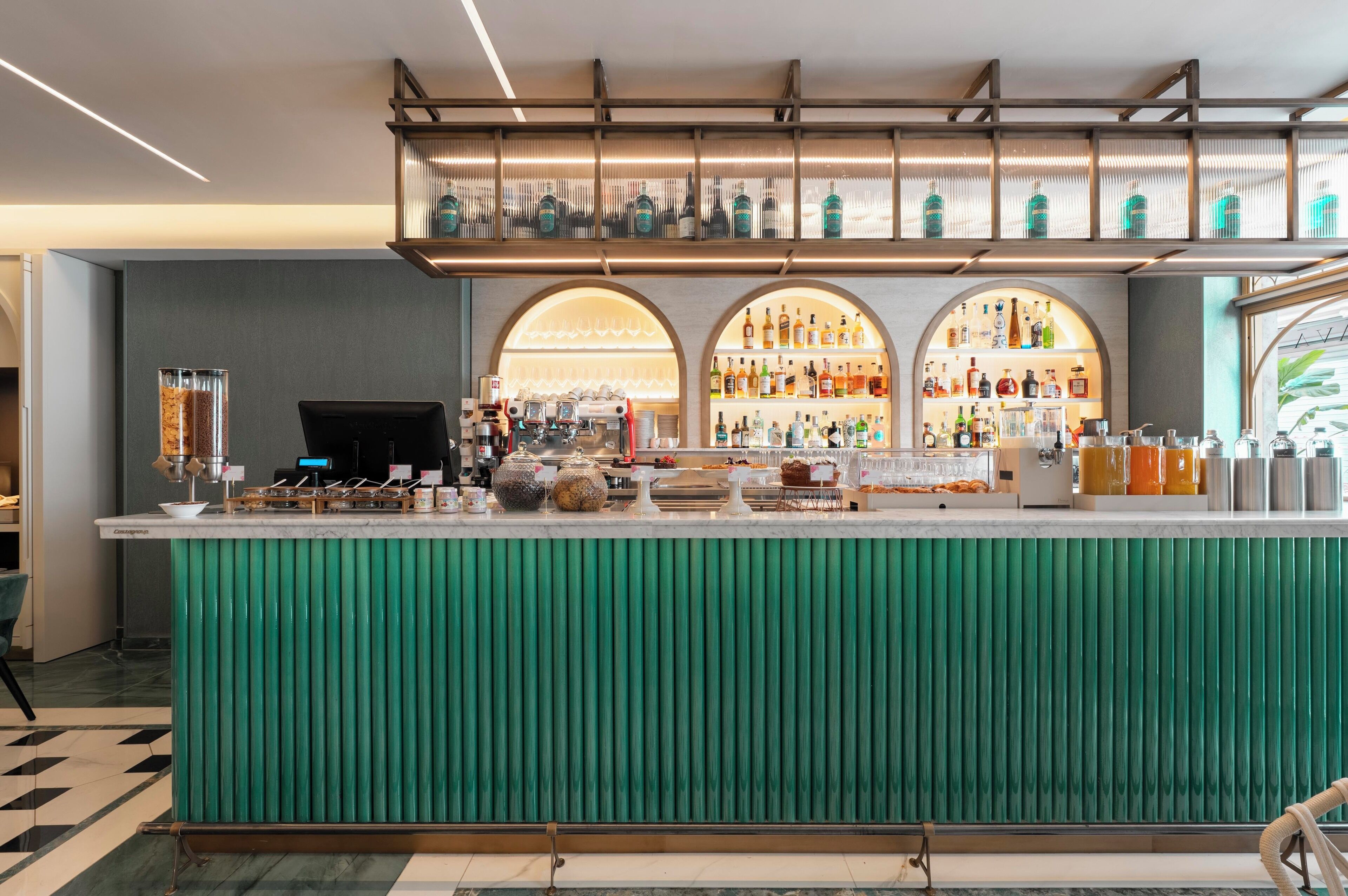A bar area with a green counter, shelves of bottles, and a coffee machine.