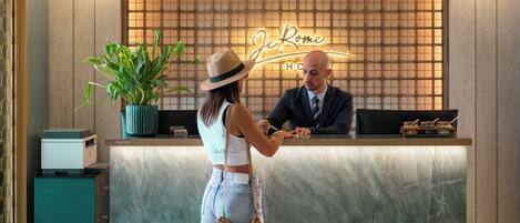 A reception desk with a neon sign reading "De Rome Hotel," a potted plant, and a check-in counter.