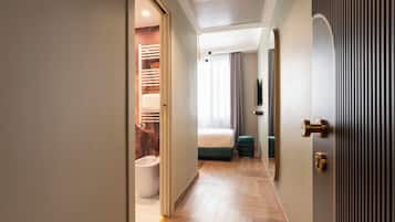 Una habitación de hotel moderna con piso de madera, una cama, un baño y un pasillo que conduce a una puerta.