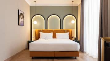 A modern hotel room with a large bed, a headboard with three light fixtures, and a bedside table with a lamp.