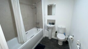A bathroom with a bathtub, a sink, a toilet, and a mirror. - New Cosy London Apartment With Garden View (London)