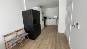 A compact kitchen with a black refrigerator, wooden bench, and white cabinets. - New Cosy London Apartment With Garden View (London)