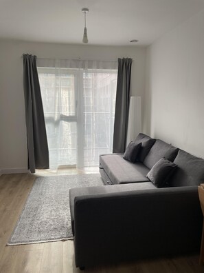A living room with a grey sofa, a patterned rug, and sheer curtains.