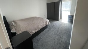 A bedroom with a bed, a desk, a wardrobe, and a window with curtains. - New Cosy London Apartment With Garden View (London)