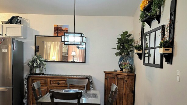 Un comedor con una mesa y sillas de madera, un ventilador de techo y una cocina al fondo.