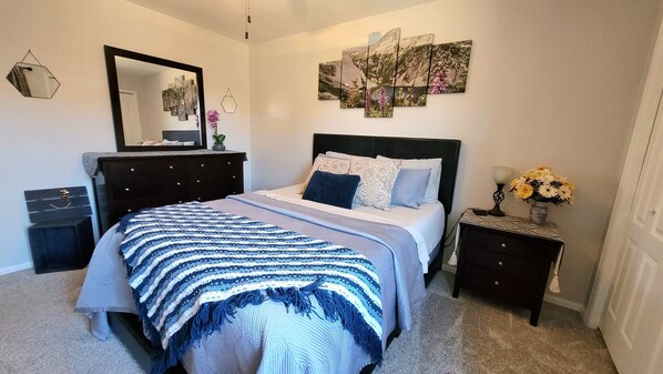 A bedroom with a bed, a dresser, a nightstand, a mirror, and wall art.