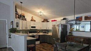 Una cocina moderna con armarios blancos, un refrigerador de acero inoxidable y un comedor con mesa y sillas.