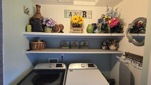 Un cuarto de lavandería con dos lavadoras Maytag, un estante con adornos y un espejo.