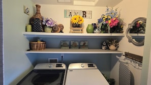 A laundry room with two Maytag washers, a shelf with decorative items, and a mirror.
