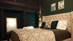 A bedroom with a tufted headboard, a patterned bedspread, and two wall-mounted artworks.