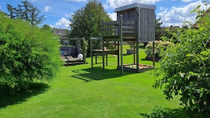 Casetta in legno con struttura per arrampicata e un piccolo giardino con prato e siepi.