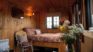 A cozy cabin room with a wooden interior, a bed with floral bedding, a chair, a radiator, and a window with a view. - Shephards Hut in the Mournes with Private Hot Tub- The Robins Nest at Willowtree (Annalong)