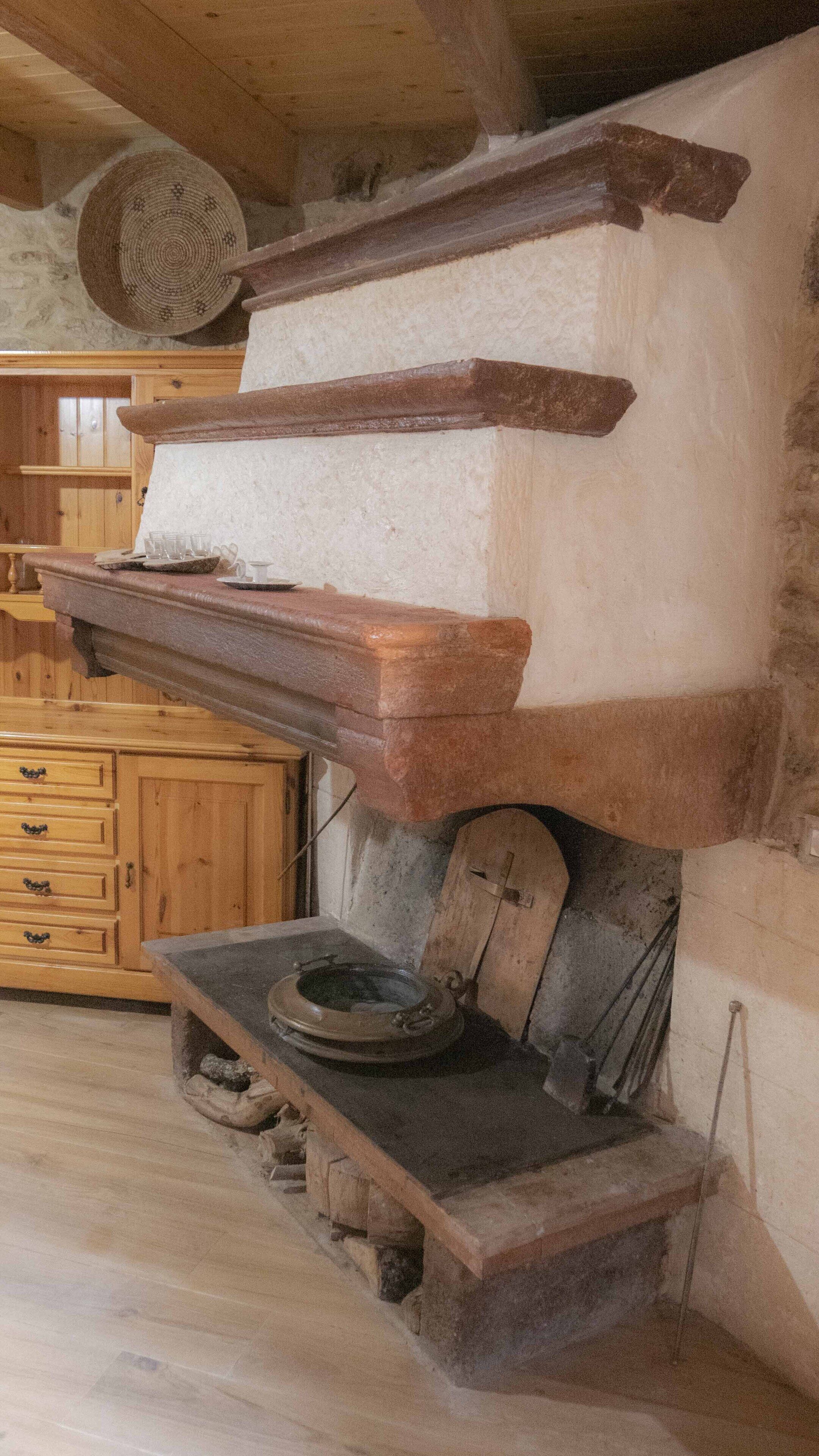 A rustic kitchen with wooden cabinets, a stone hearth, and a large woven basket.