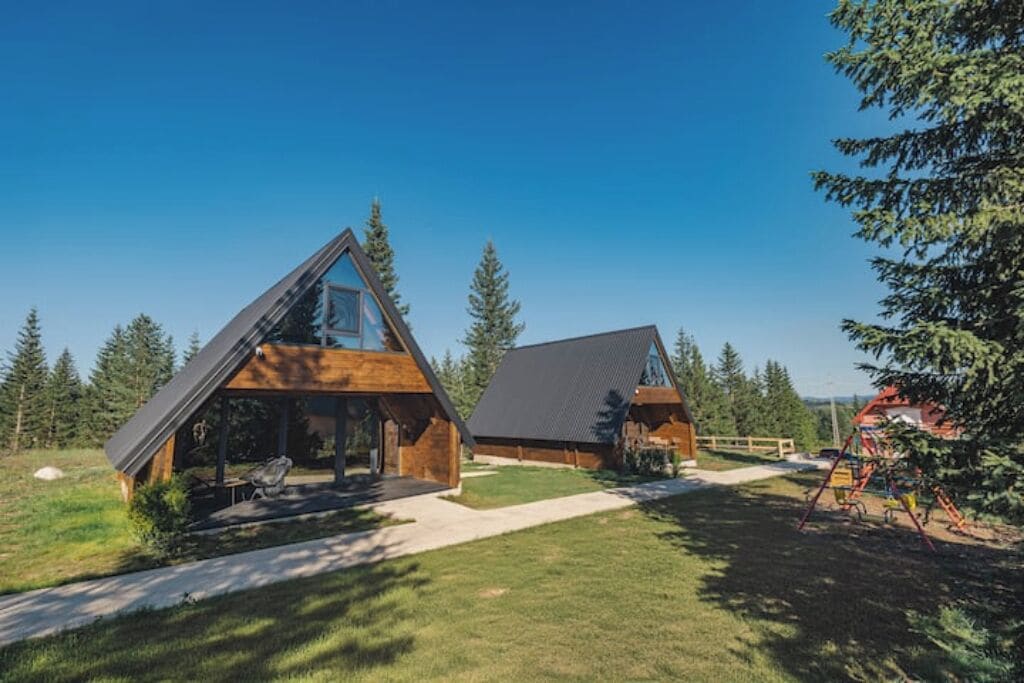 Eine moderne Hütte mit geneigtem Dach, großen Fenstern und einer Holzfassade.