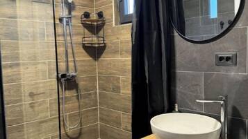 A modern bathroom with a glass-enclosed shower, a round mirror, and a white sink on a wooden vanity.