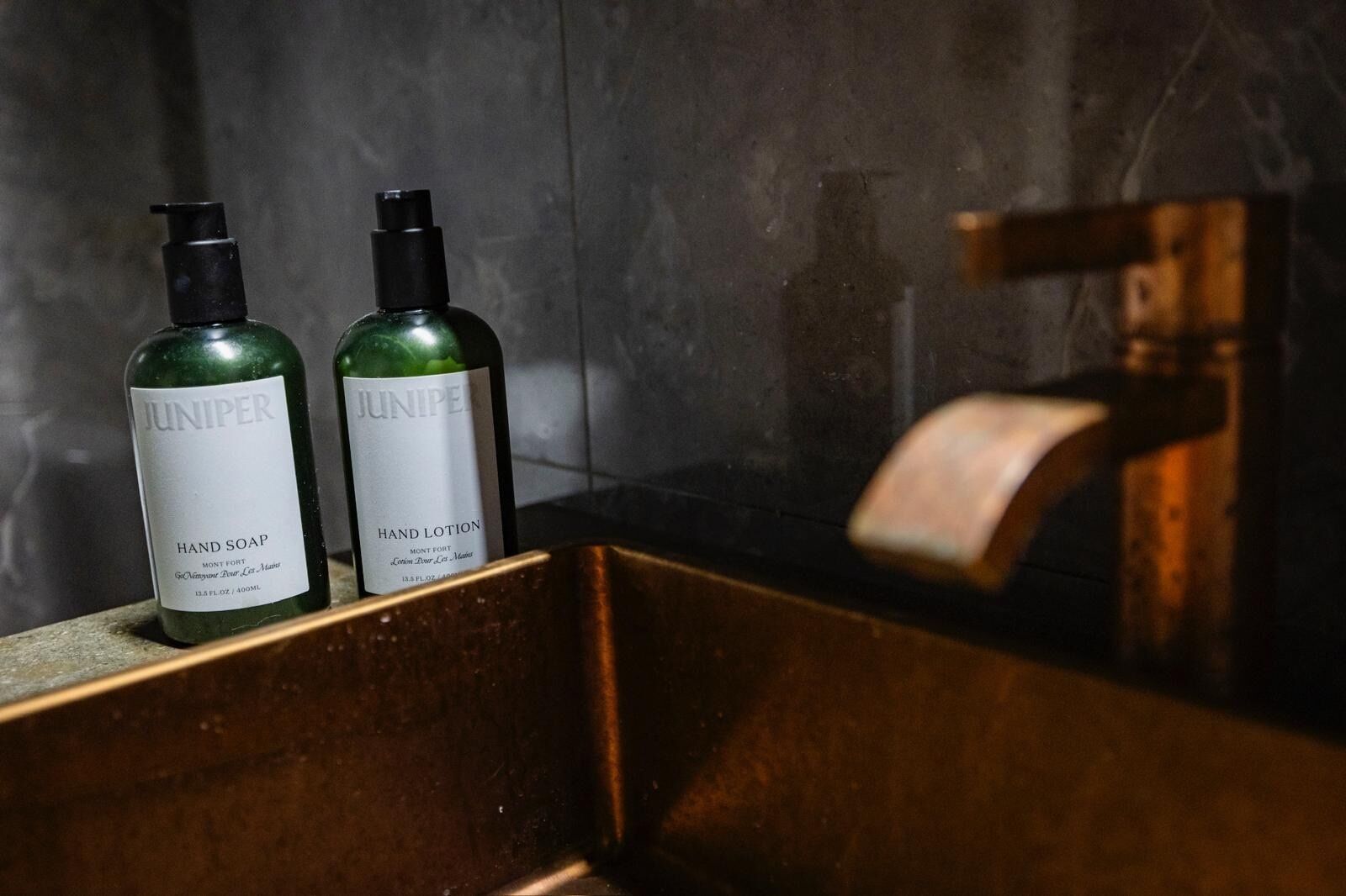 Zwei Flaschen Juniper Handseife und Handlotion auf einer metallischen Oberfläche.