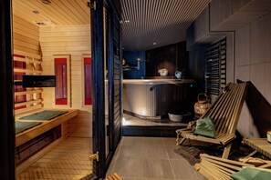 A sauna room with wooden benches, a massage table, and a steam room with a bench and a small table. - The Private Escape by Blue Medi Spa (Stockholm)