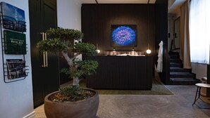 A reception area with a large potted tree, a wall-mounted clock, and a framed artwork. - The Private Escape by Blue Medi Spa (Stockholm)