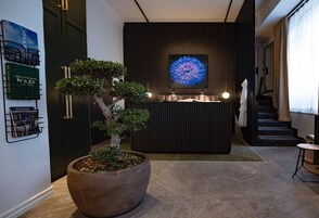 Un área de recepción con un gran árbol en maceta, un reloj de pared y una obra de arte enmarcada.