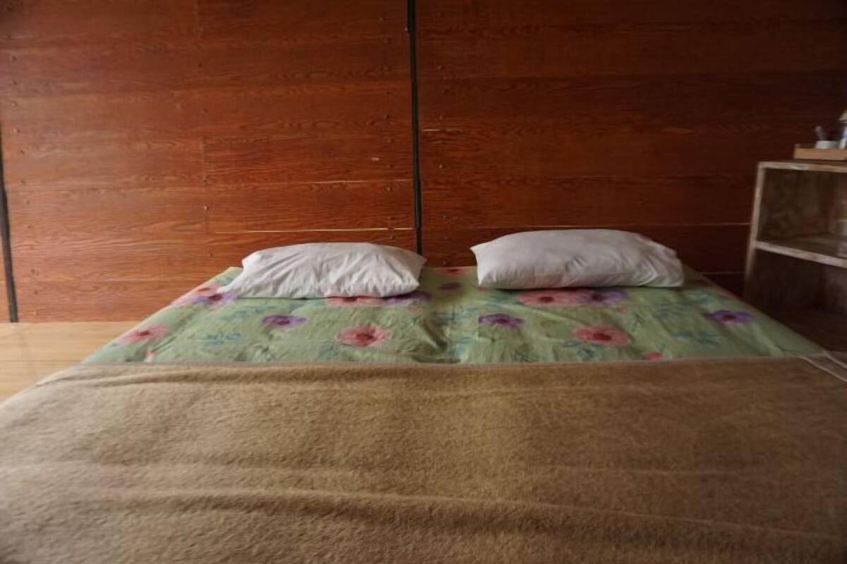 A bed with a floral bedspread and two pillows, a wooden wall, and a small wooden shelf.