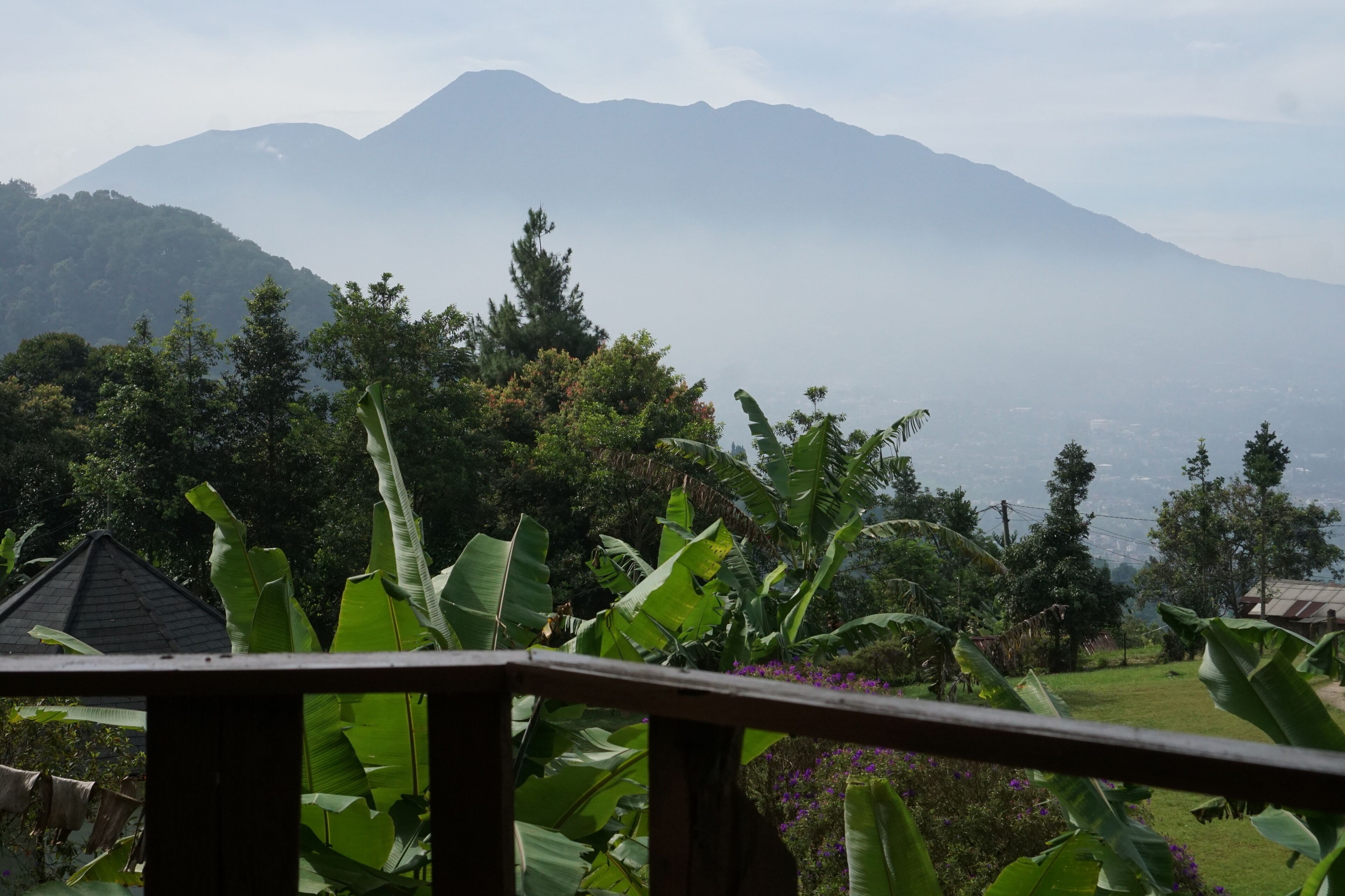 A view of mountains, lush greenery, and a house with a sloped roof.