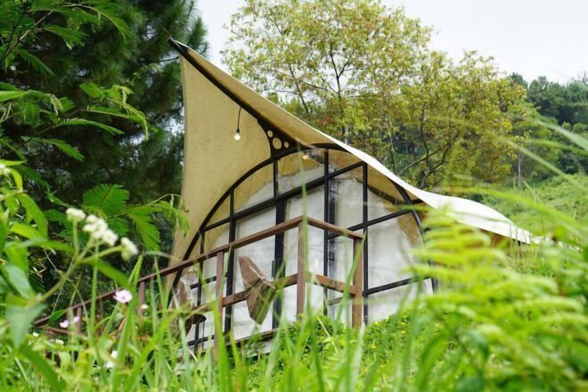 A small, rustic cabin-like structure with a sloped roof, surrounded by lush greenery and trees.