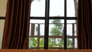 Una ventana con vista a follaje y barandilla de madera.