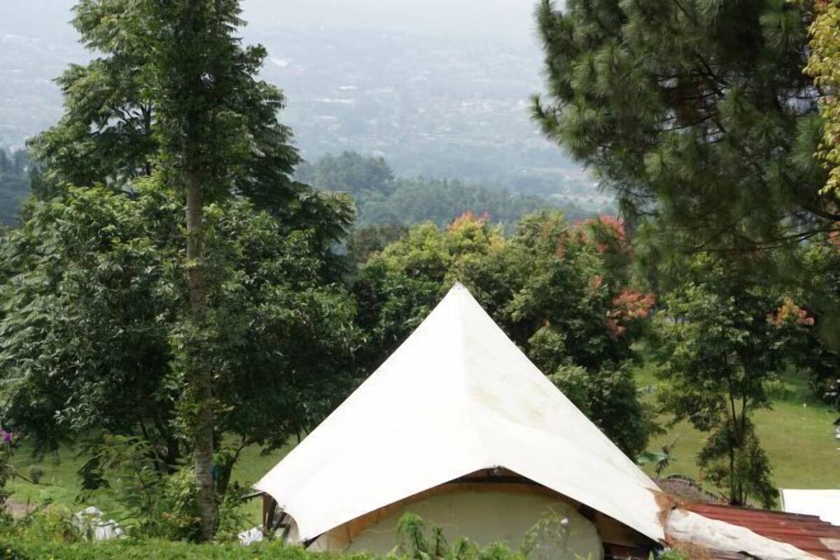 A house with a triangular roof, surrounded by trees and a hilly landscape.