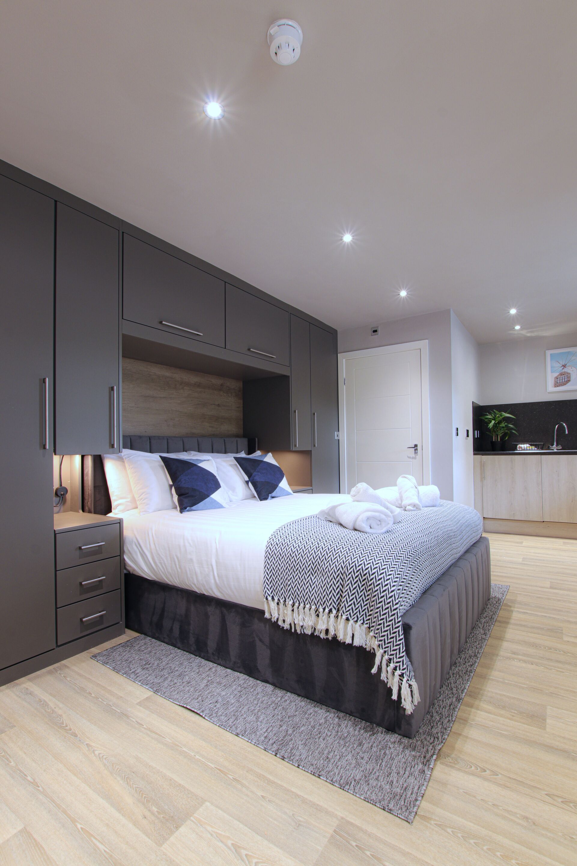 Un dormitorio moderno con una cama grande, armarios grises, una mesita de noche pequeña y un banco empotrado.