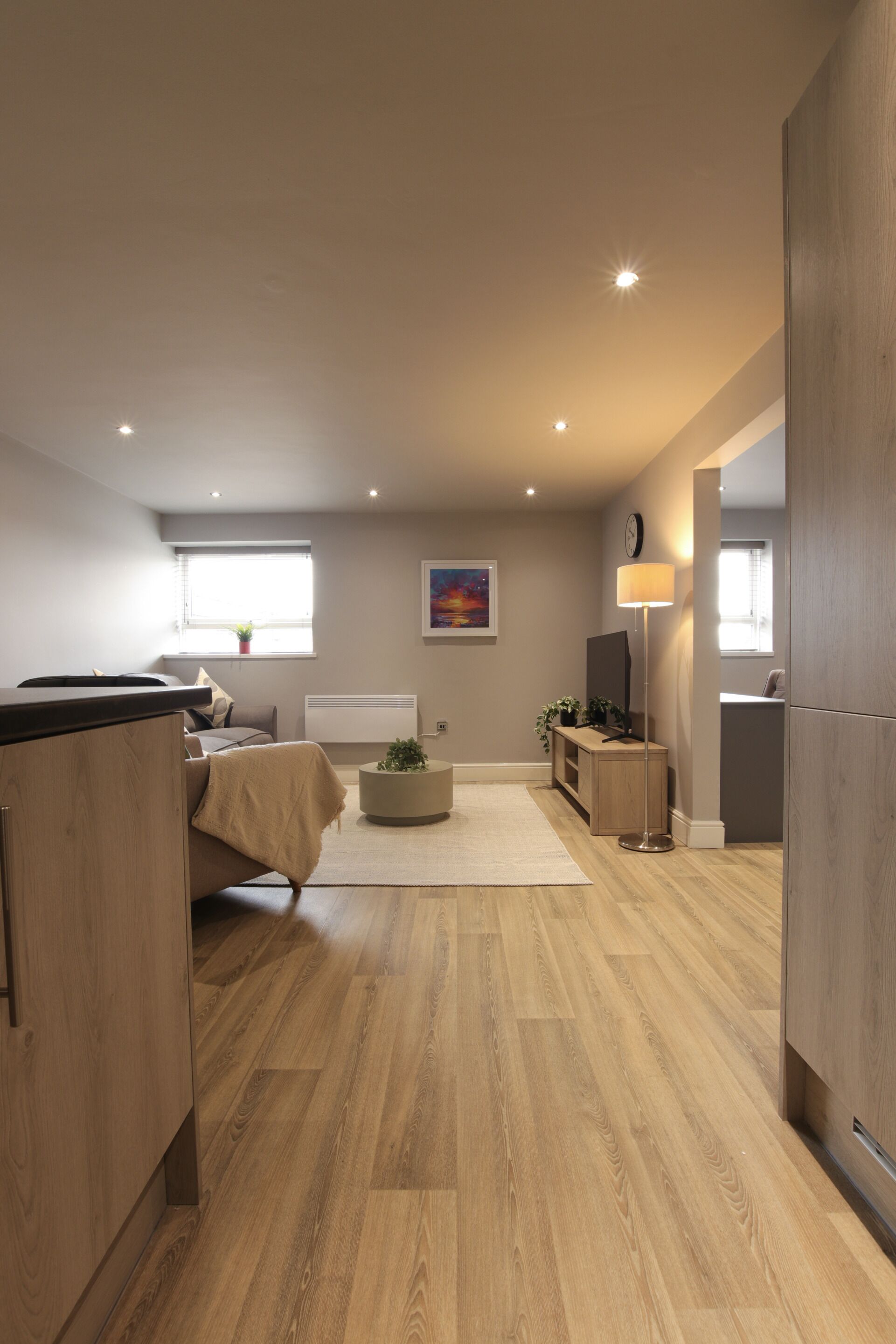 Una habitación moderna y bien iluminada con piso de madera, una cama, un escritorio y una lámpara.
