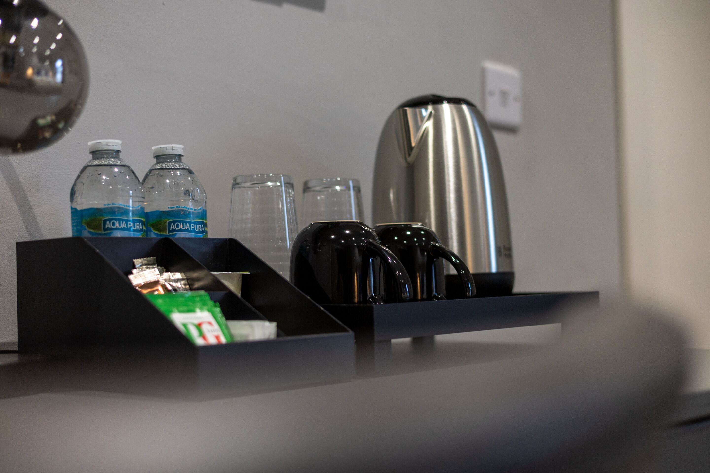 A hotel minibar with water bottles, glasses, a coffee maker, and a tea kettle.