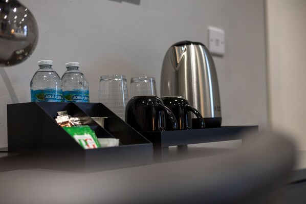 A hotel minibar with water bottles, glasses, a coffee maker, and a tea kettle. - The Ironworks Aparthotel (Telford)