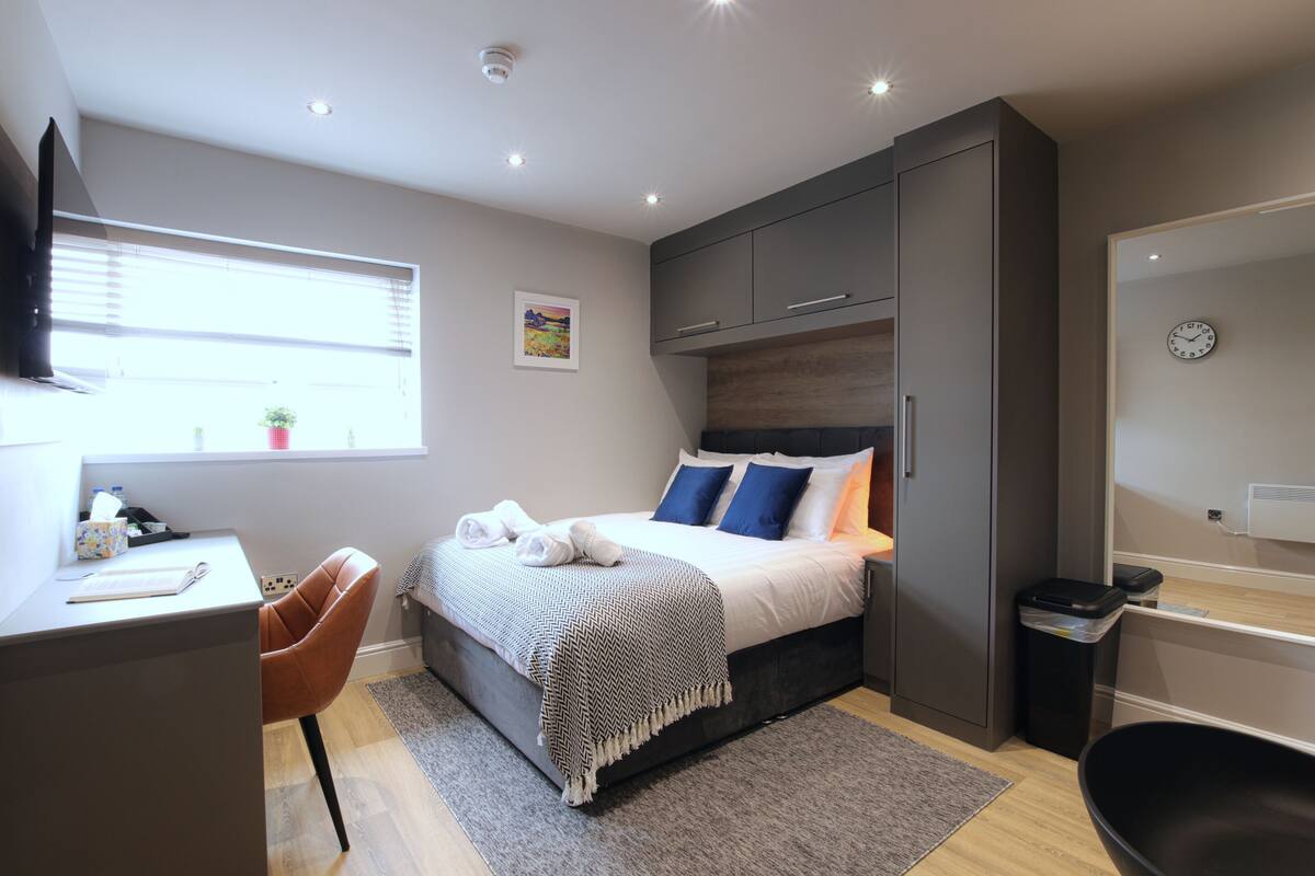A modern bedroom with a bed, desk, chair, and a small window.