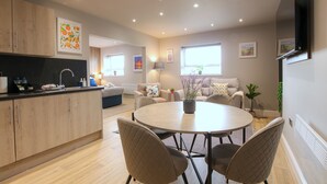 Une cuisine moderne avec des meubles en bois, un coin repas avec une table ronde et des chaises, et un salon avec un canapé et un téléviseur.
