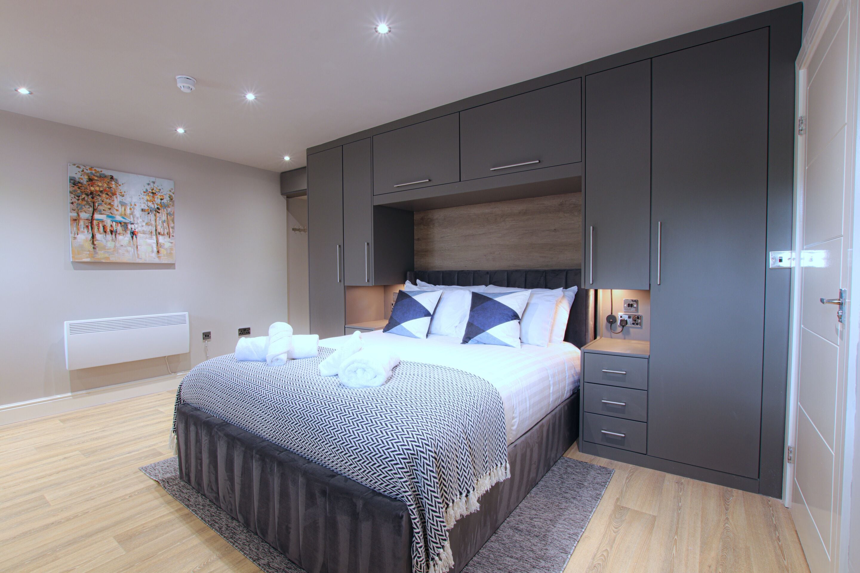 Une chambre moderne avec un grand lit, des armoires grises et un tableau au mur.