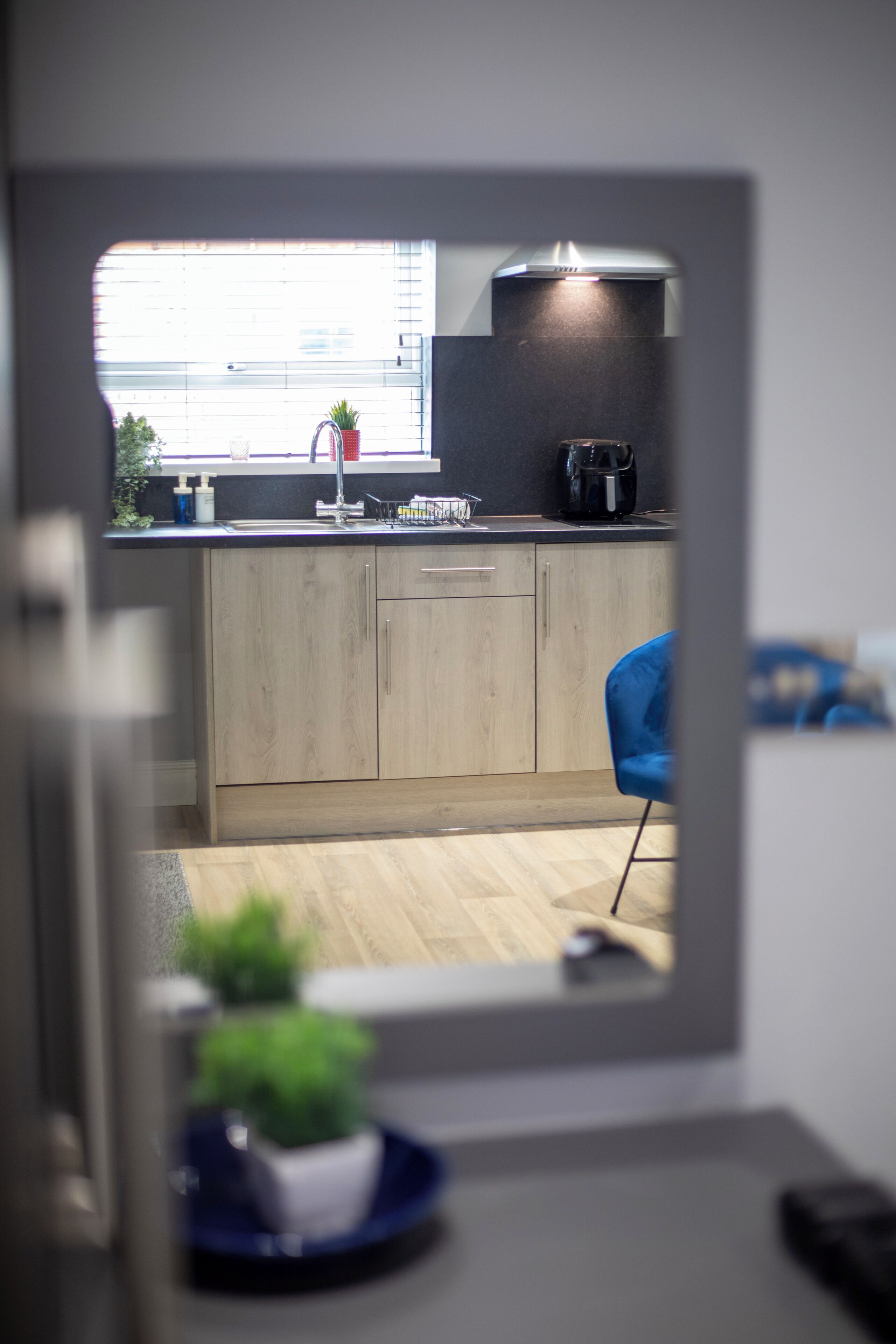 A modern kitchen with wooden cabinets, a sink, and a coffee maker. There is a blue chair and a small potted plant on the counter.