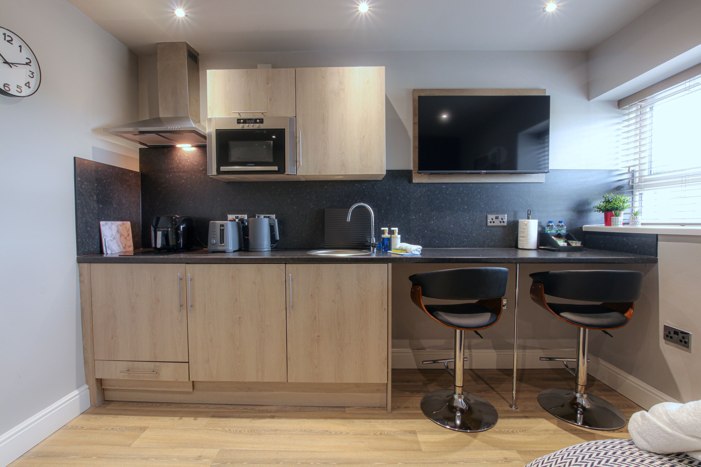 A modern kitchen with wooden cabinets, a microwave, a sink, and two bar stools.