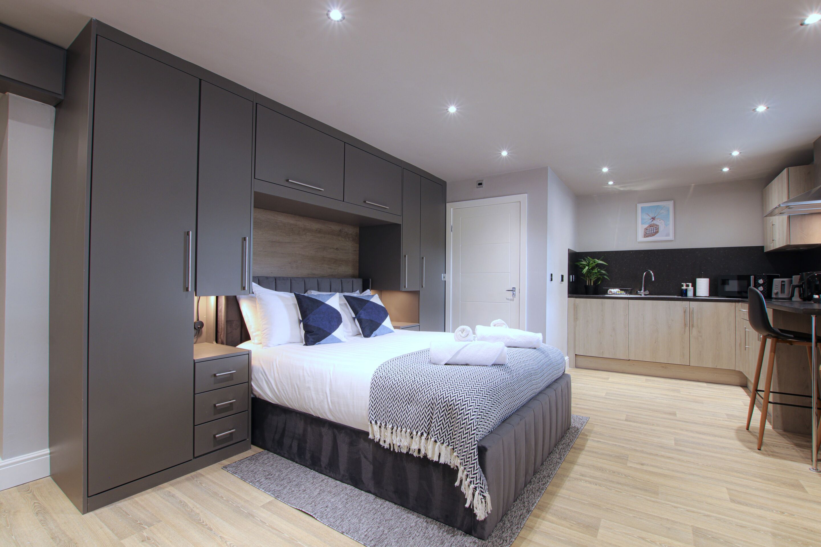 A modern bedroom with a large bed, built-in wardrobe, and a separate kitchenette area.